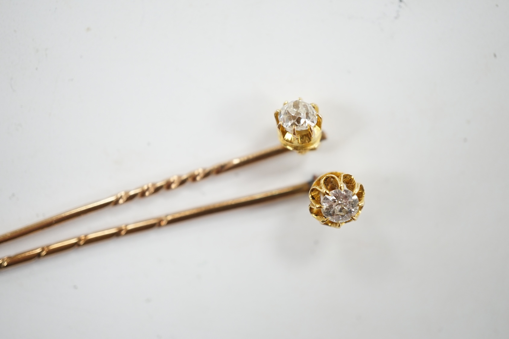 Two early 20th century yellow metal and solitaire diamond set stick pins, 65mm and a dress stud. Condition - fair to good